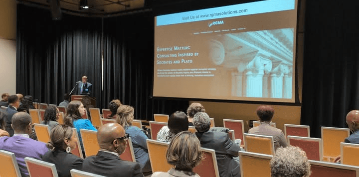 Attendees seated in an auditorium watching a presenter at a podium during an OMSDC business session